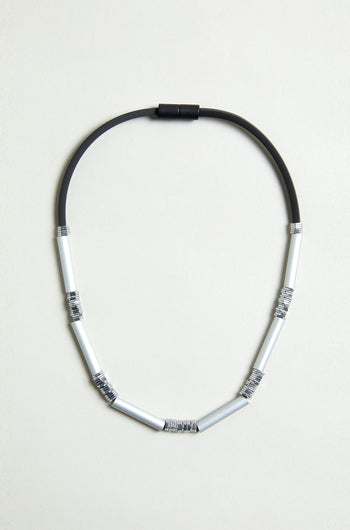 The Silver Aluminium Hematite Necklace is a contemporary design by Christina Brampti, featuring black rubber and six silver anodised aluminium segments wrapped in thin wire, shown on a plain light background.
