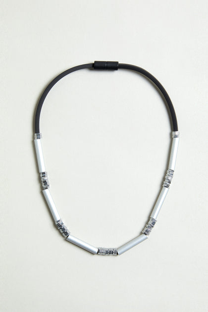 The Silver Aluminium Hematite Necklace is a contemporary design by Christina Brampti, featuring black rubber and six silver anodised aluminium segments wrapped in thin wire, shown on a plain light background.