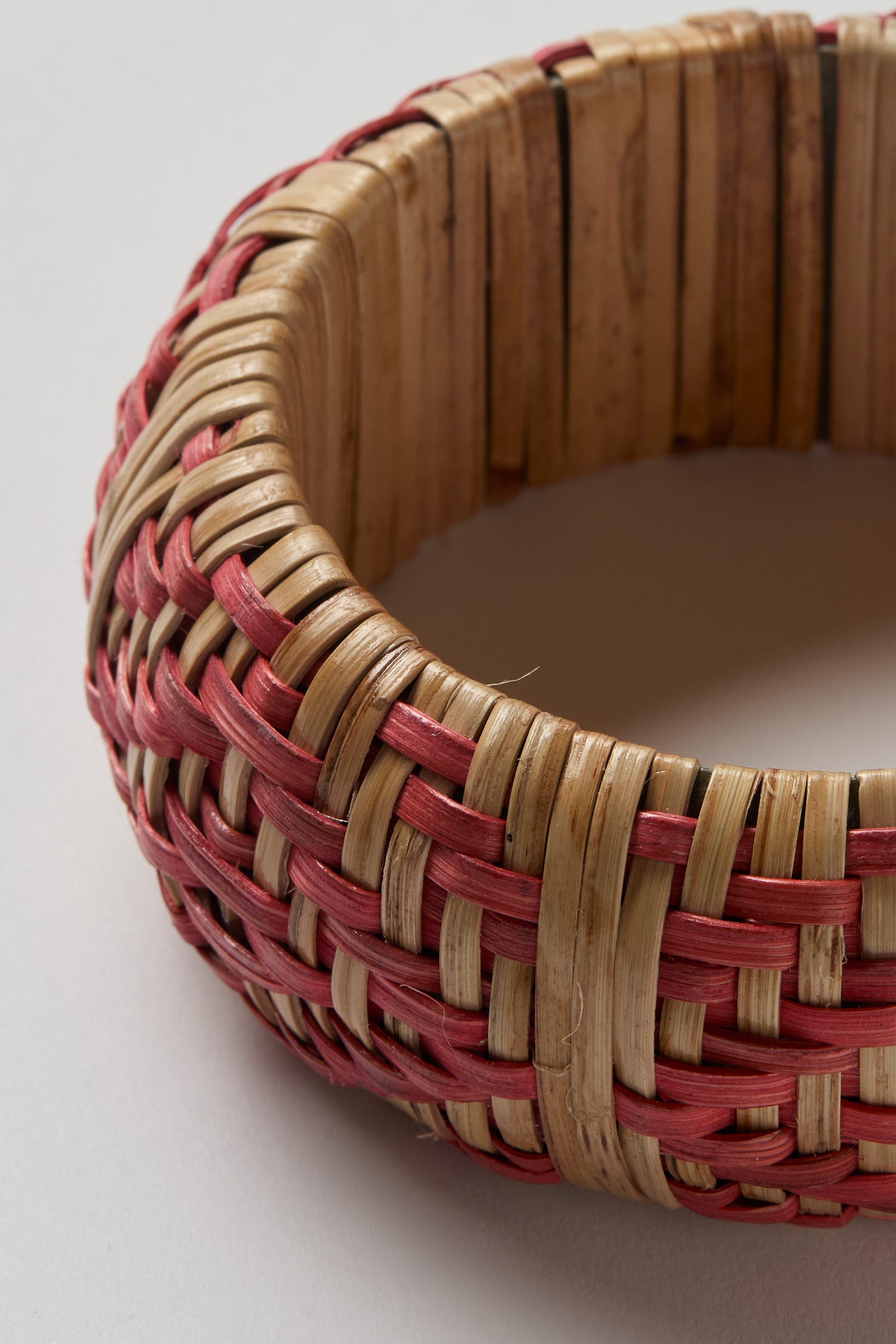 A close-up of the Handwoven Rose Rattan Bangle showcases its natural and red fibers, intricate texture, fine craftsmanship, and rich artisanal tradition.