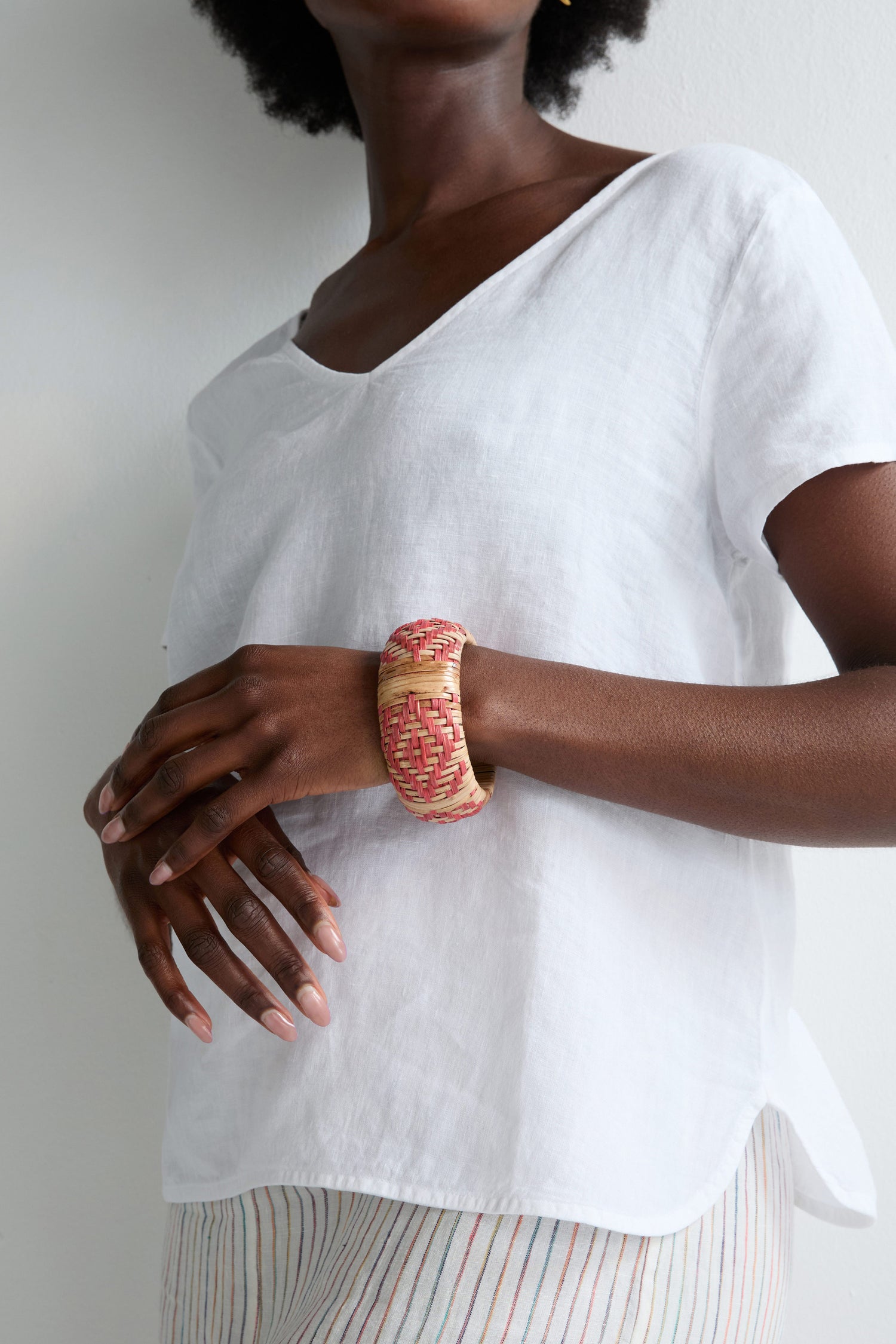 Wearing a loose white shirt and striped pants, someone showcases the Handwoven Rose Rattan Bangle on their wrist, highlighting its natural beauty and artisanal craftsmanship.