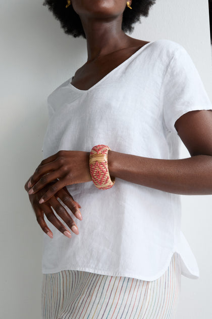Wearing a loose white shirt and striped pants, someone showcases the Handwoven Rose Rattan Bangle on their wrist, highlighting its natural beauty and artisanal craftsmanship.