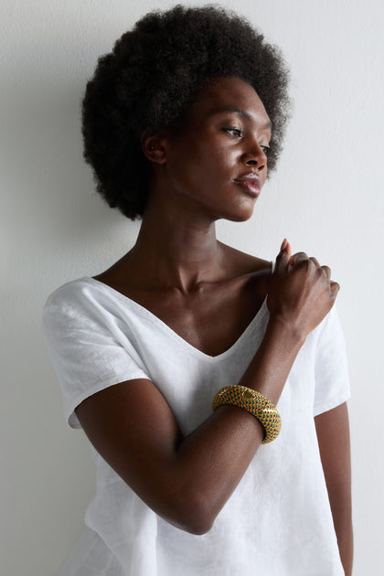 A woman with a natural afro and white top showcases the Handwoven Multicoloured Bangle against a plain white background, celebrating heritage craftsmanship.