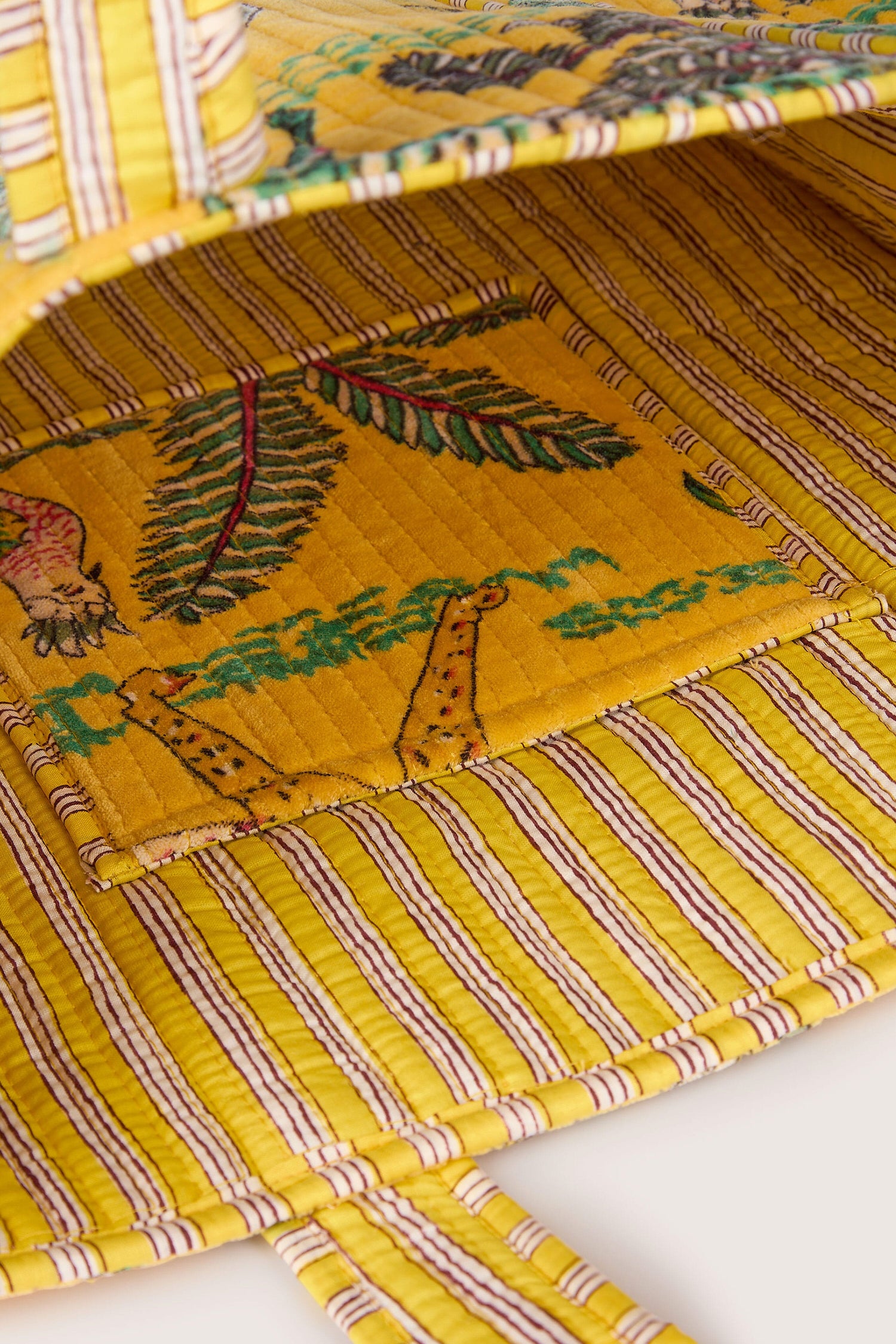 Close-up of an open, yellow Jungle Print Velvet Bag with striped patterns and botanical designs on the inside flap.