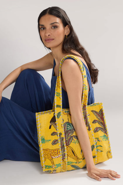 A woman in a blue dress sits with a Jungle Print Velvet Bag draped over her shoulder.