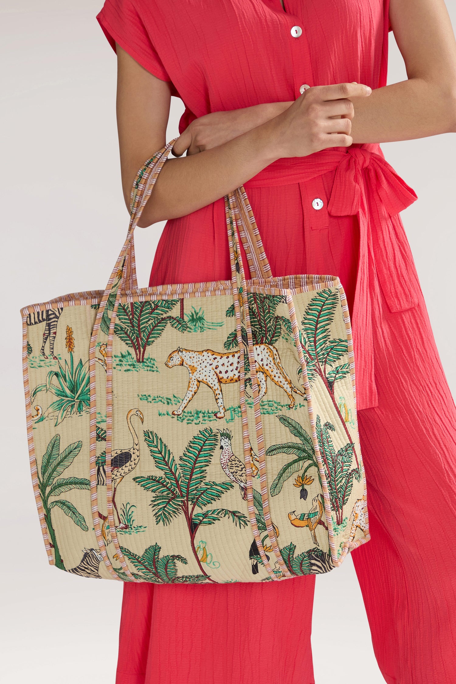 Person in a bright red outfit holding a Jungle Print Tote Bag against a plain background.