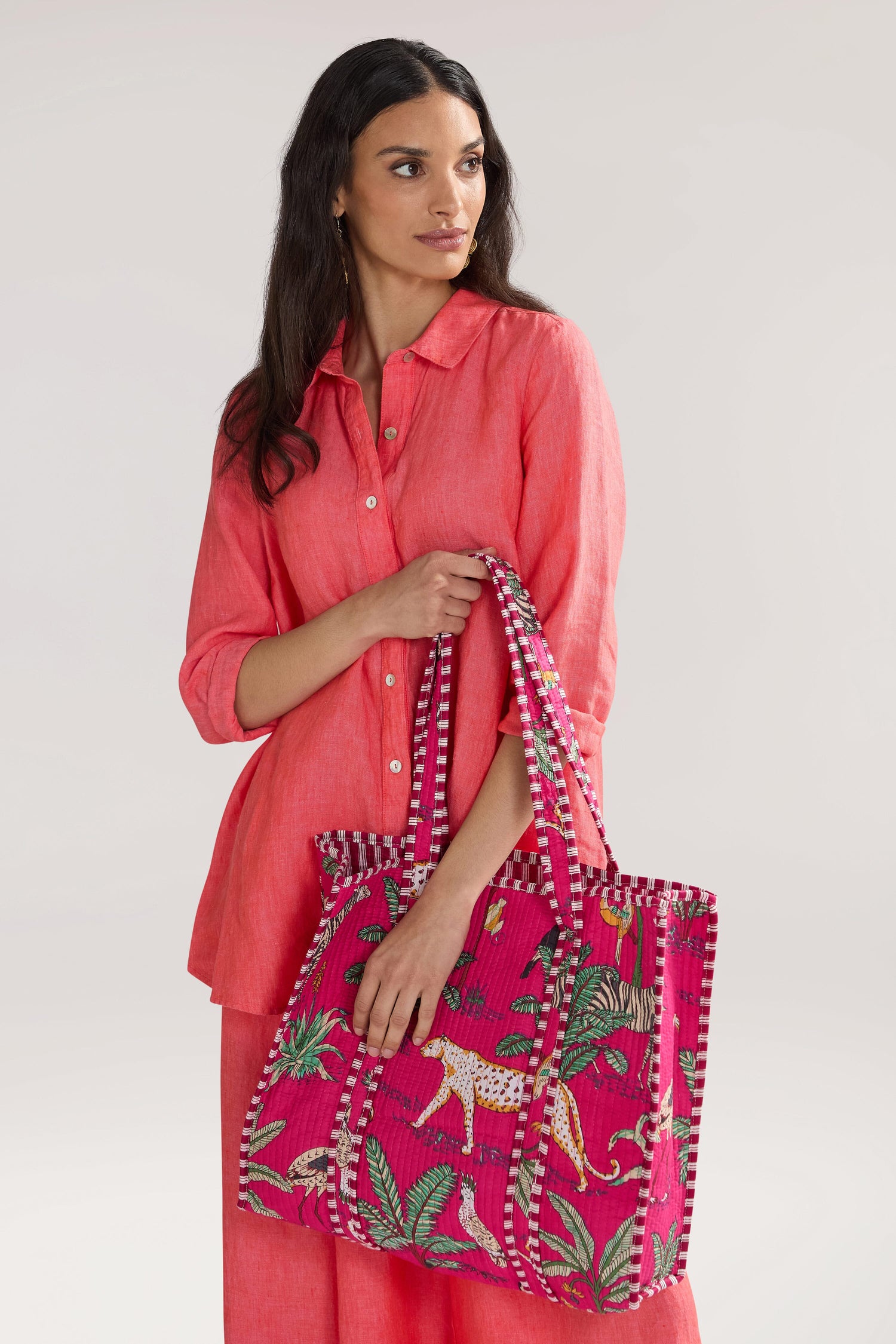 A person in a coral shirt and pants holds a bright pink patterned Jungle Print Tote Bag with a design featuring a cheetah and tropical foliage.