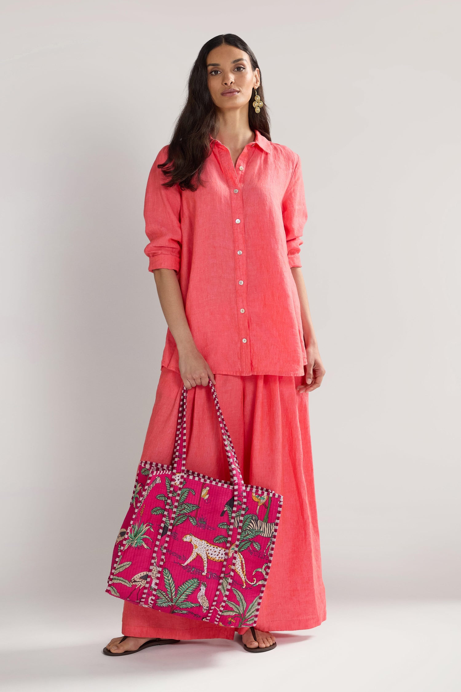 A woman in a coral button-down shirt and matching skirt holds a Jungle Print Tote Bag. She has long, dark hair and wears dangling earrings.

Since the provided sentence already contains the product name "Jungle Print Tote Bag," no changes are necessary.