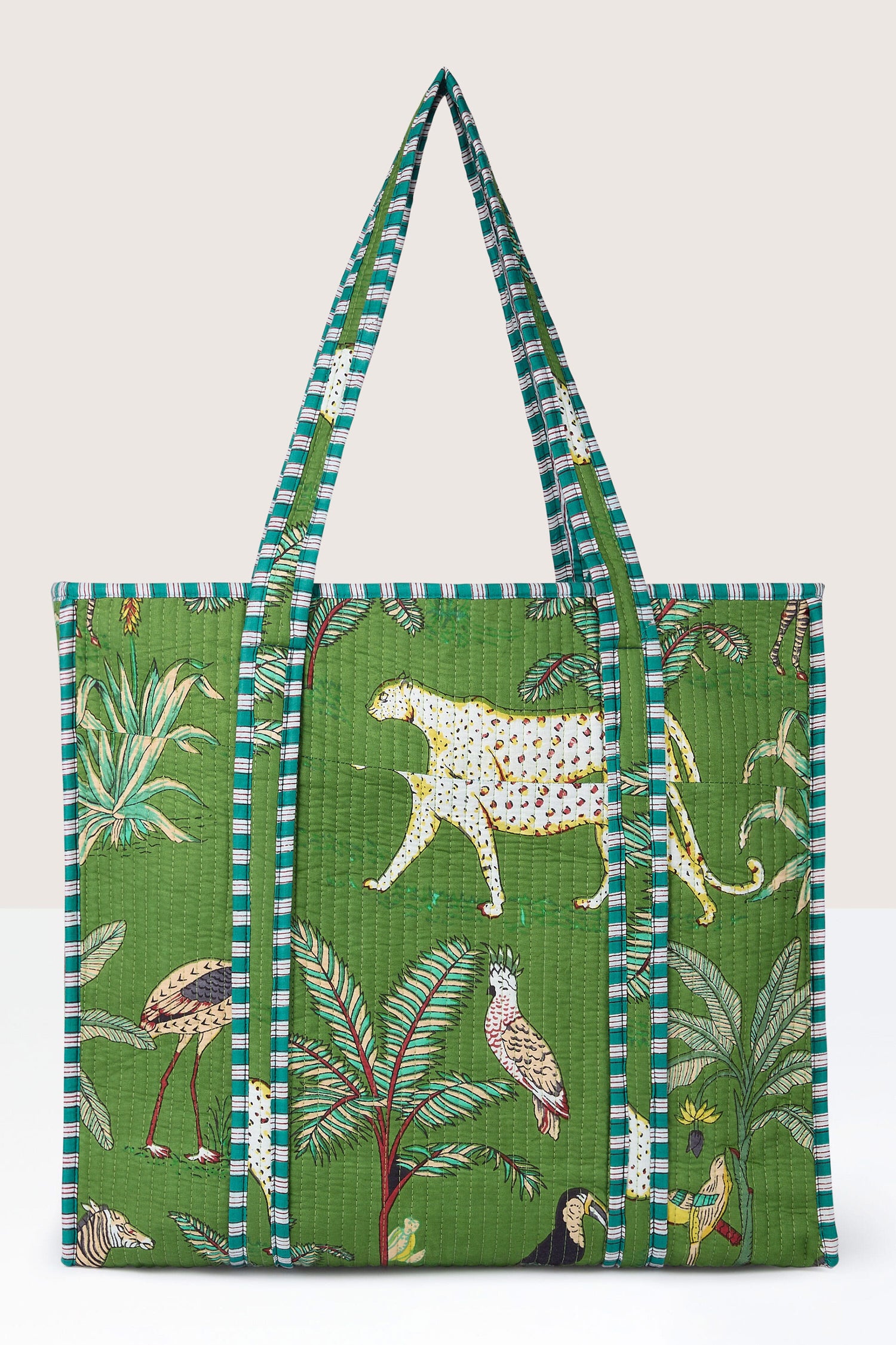 The Jungle Print Tote Bag, made with quilted fabric, showcases vibrant animals and plants. Its green design is complemented by striped handles and edges, ideal for the eco-friendly shopper.