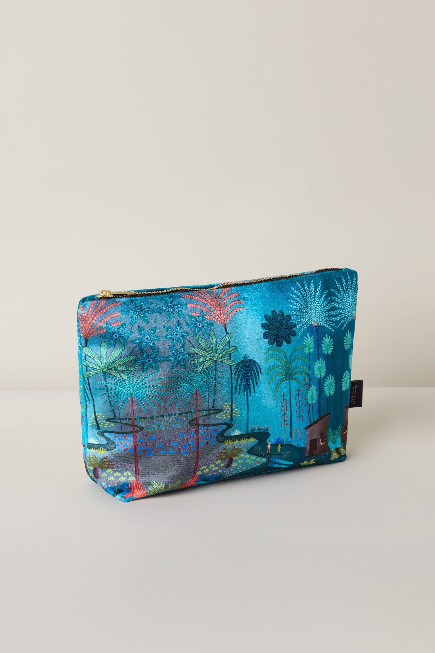 The Large Jungle Pathway Velvet Bag highlights a vibrant nature-themed design by Daphne Stephenson, showcasing trees, plants, and water on a blue backdrop.