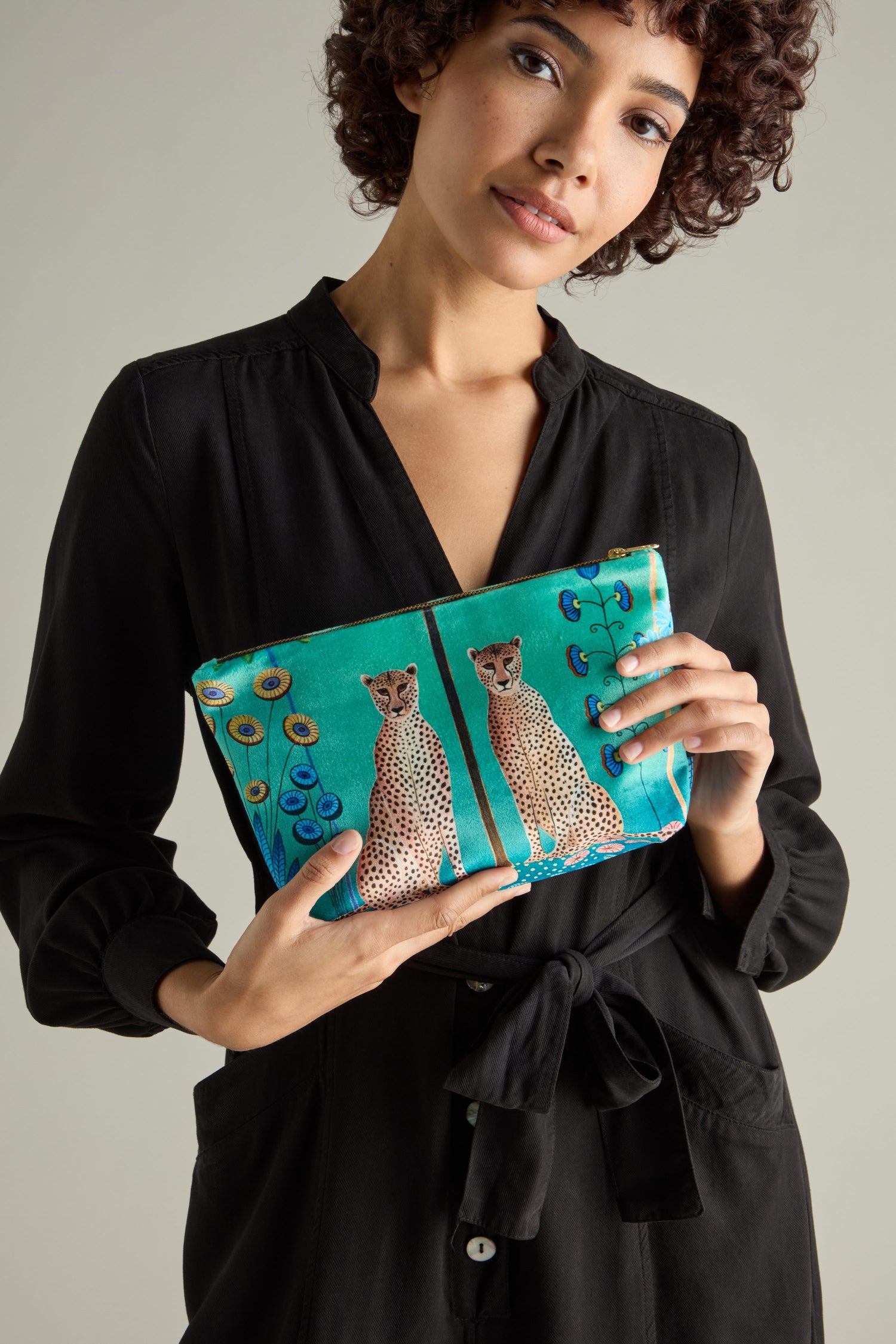 A person in a black dress holds a turquoise Large Sunshine Through My Window Velvet Bag adorned with cheetah illustrations.