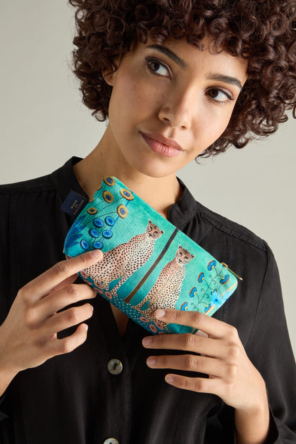 The person, in a black shirt, confidently holds the Small Sunshine Through My Window Velvet Bag with a stunning teal clutch design featuring cheetahs and intricate peacock feathers.