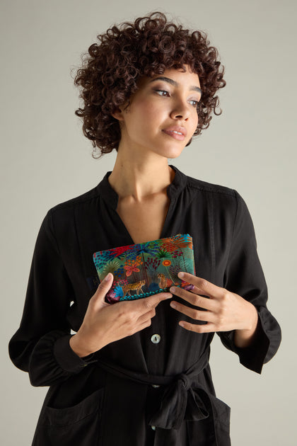 A person with curly hair displays a colorful, patterned Small Tale of Two Tigers Velvet Bag against their black buttoned dress on a neutral background, capturing the vibrant artistry of Daphne Stephenson.