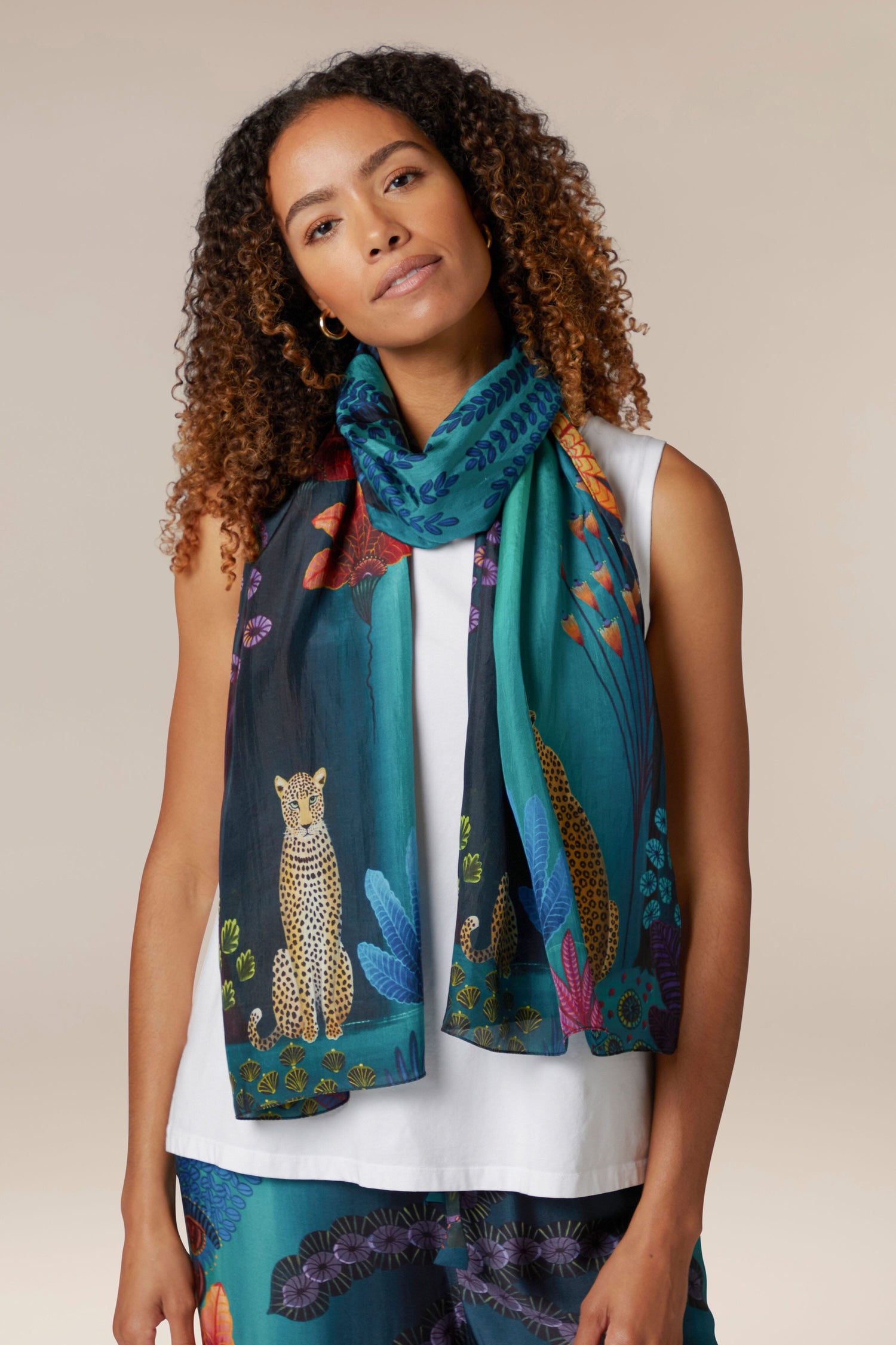 A woman wearing the Twilight Jungle Silk Scarf, sourced ethically, with a leopard print on it.