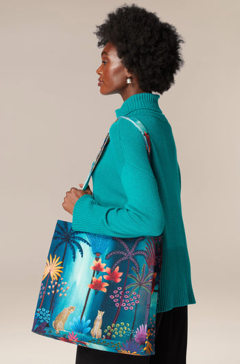 A woman holding a Twilight Jungle Tote Bag with a tropical print featuring jungle scenes.