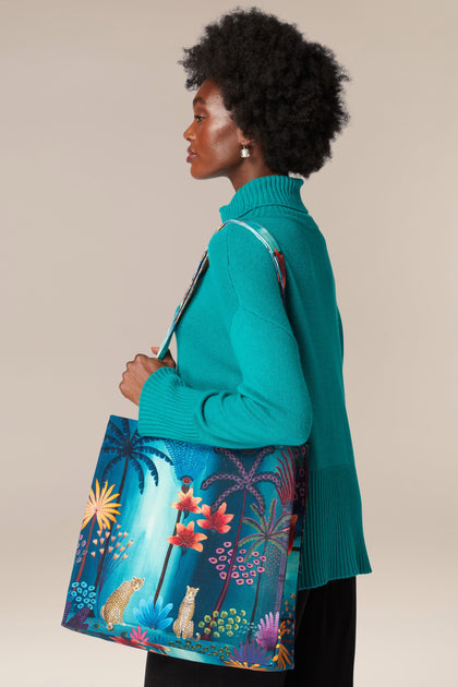 A woman holding a Twilight Jungle Tote Bag with a tropical print featuring jungle scenes.