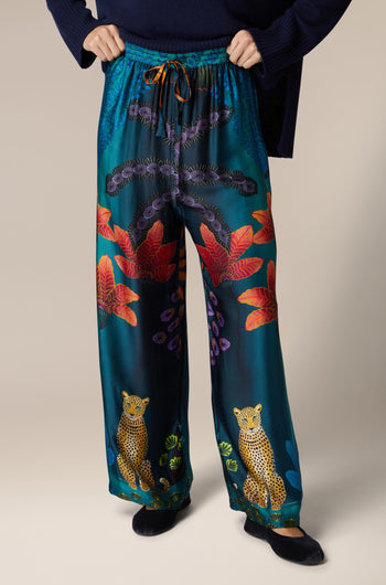 A woman wearing Twilight Jungle Trousers, which are wide-leg silk trousers with an exotic animal print.