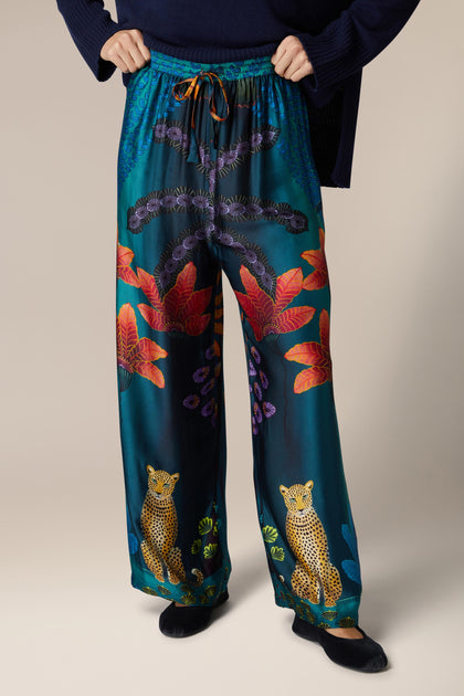 A woman wearing Twilight Jungle Trousers, which are wide-leg silk trousers with an exotic animal print.