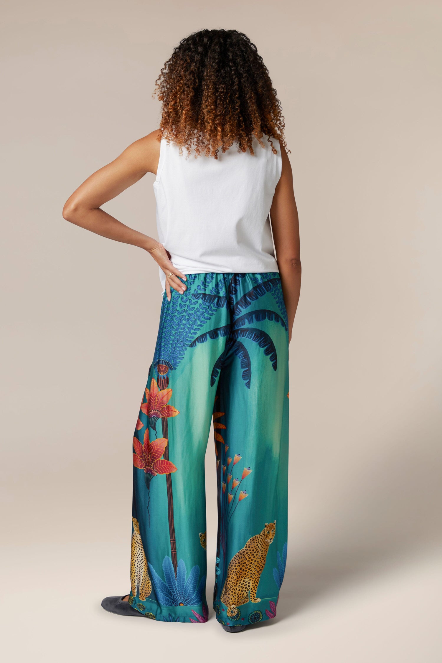 The back view of a woman wearing Twilight Jungle Trousers with a tropical print and an elasticated waistband.