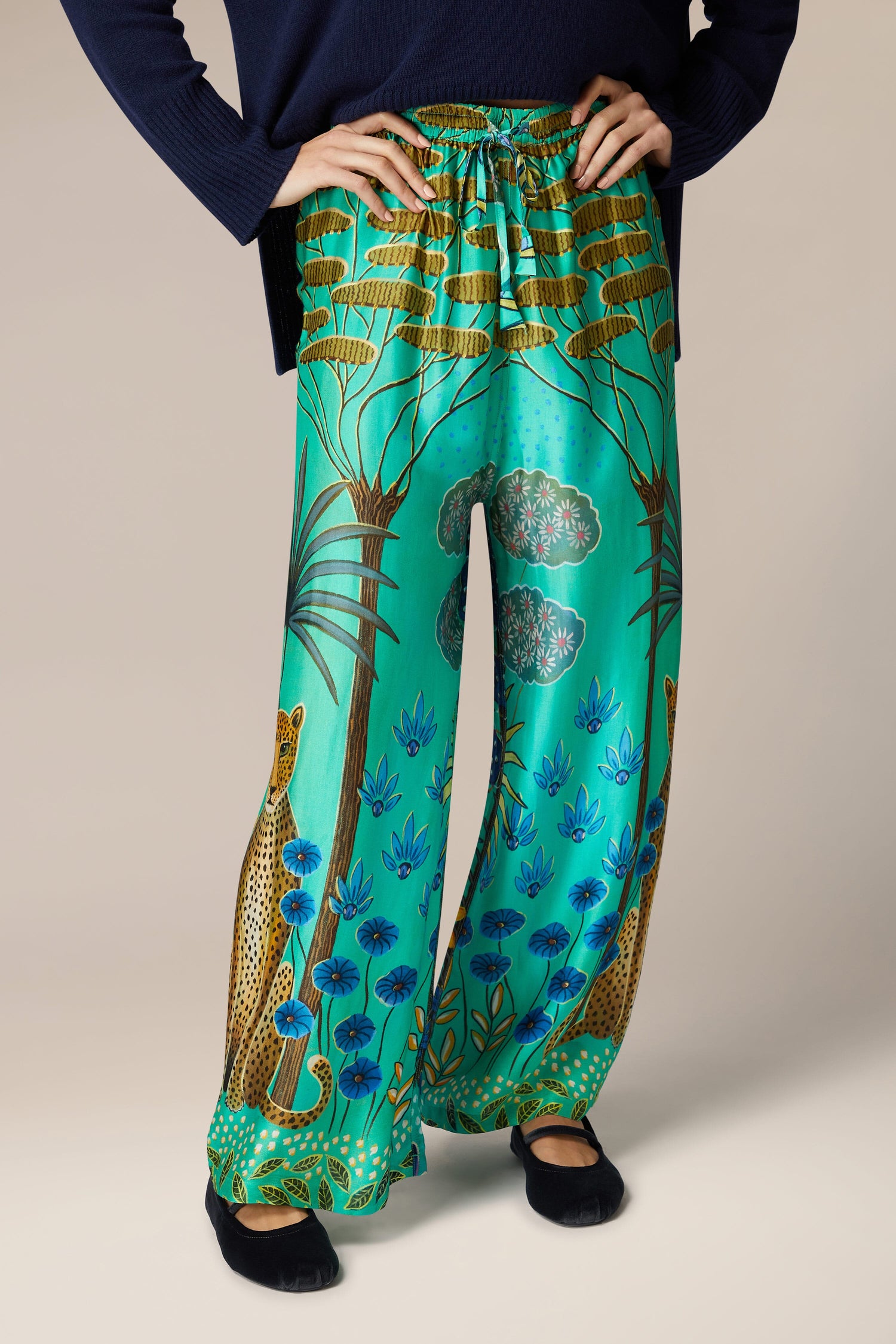 A woman wearing Leopard in Moonlight Trousers, wide-leg trousers in a green silk pant with a print of a tiger, exuding an exotic style.