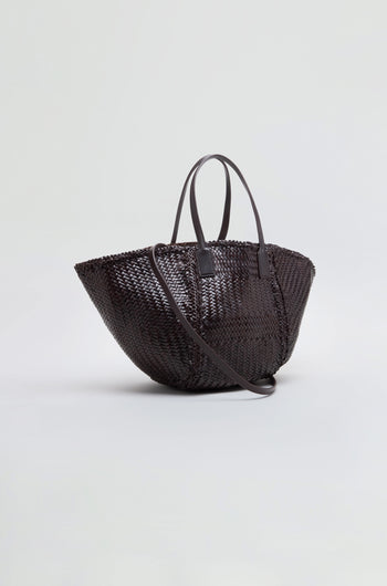 The Teresa Woven Leather Bag, crafted using traditional weaving techniques in dark brown leather, features two top handles and a long shoulder strap, and is displayed on a plain light background.