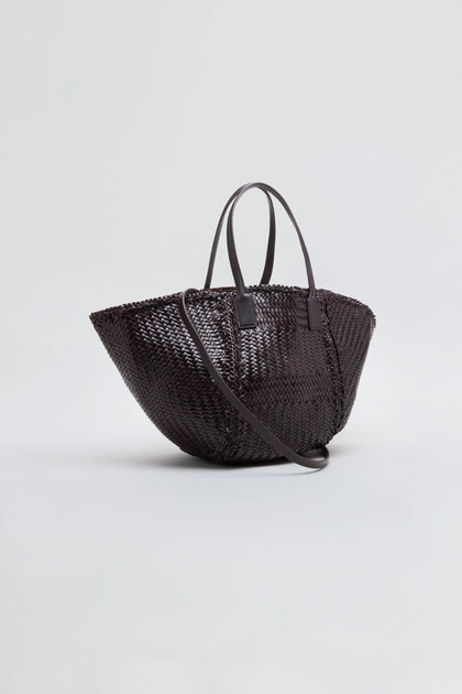 The Teresa Woven Leather Bag, crafted using traditional weaving techniques in dark brown leather, features two top handles and a long shoulder strap, and is displayed on a plain light background.