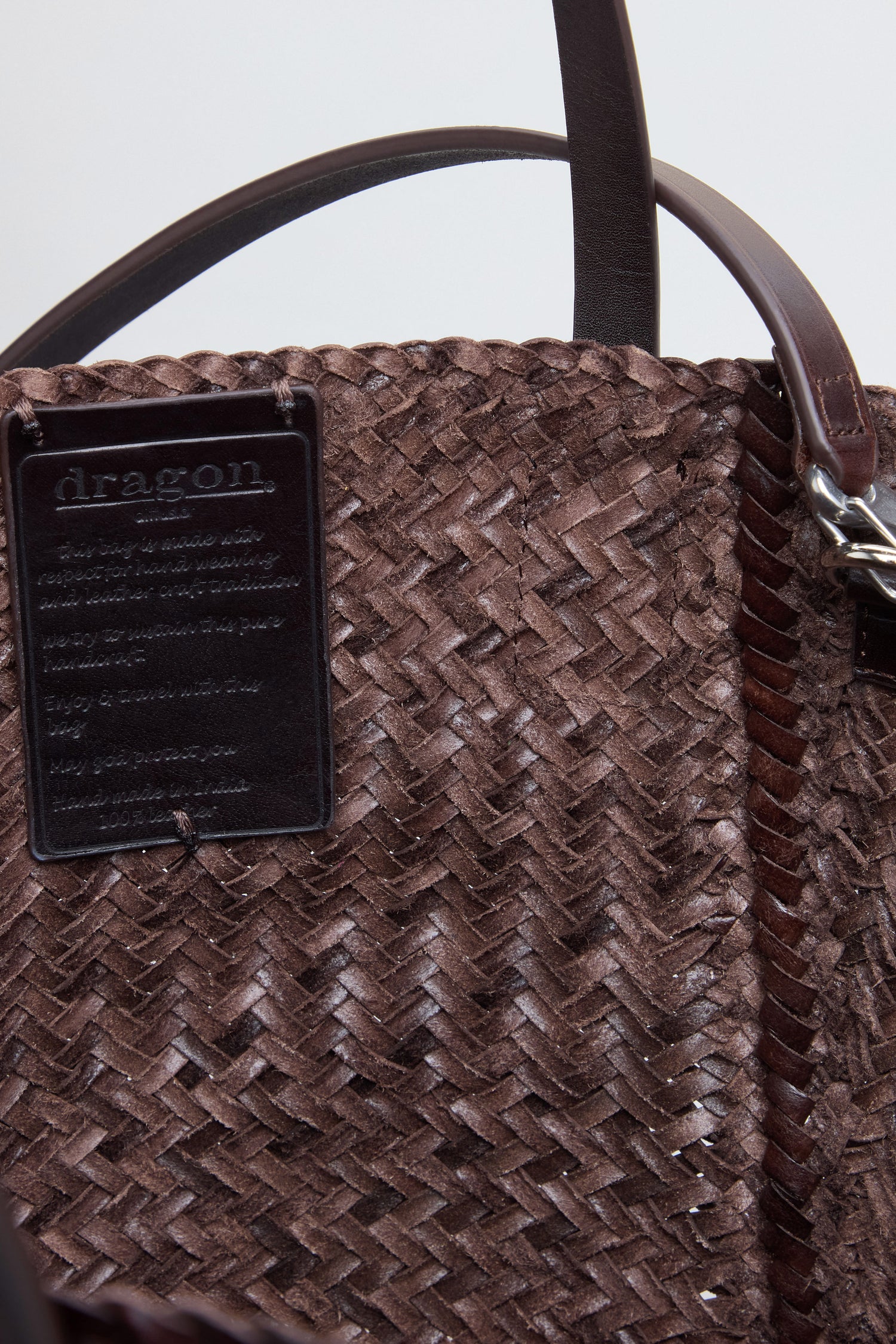 Close-up of the Teresa Woven Leather Bag, a brown woven leather bag expertly crafted with traditional weaving techniques, featuring two handles and a black rectangular label reading "dragon." attached on the inside.
