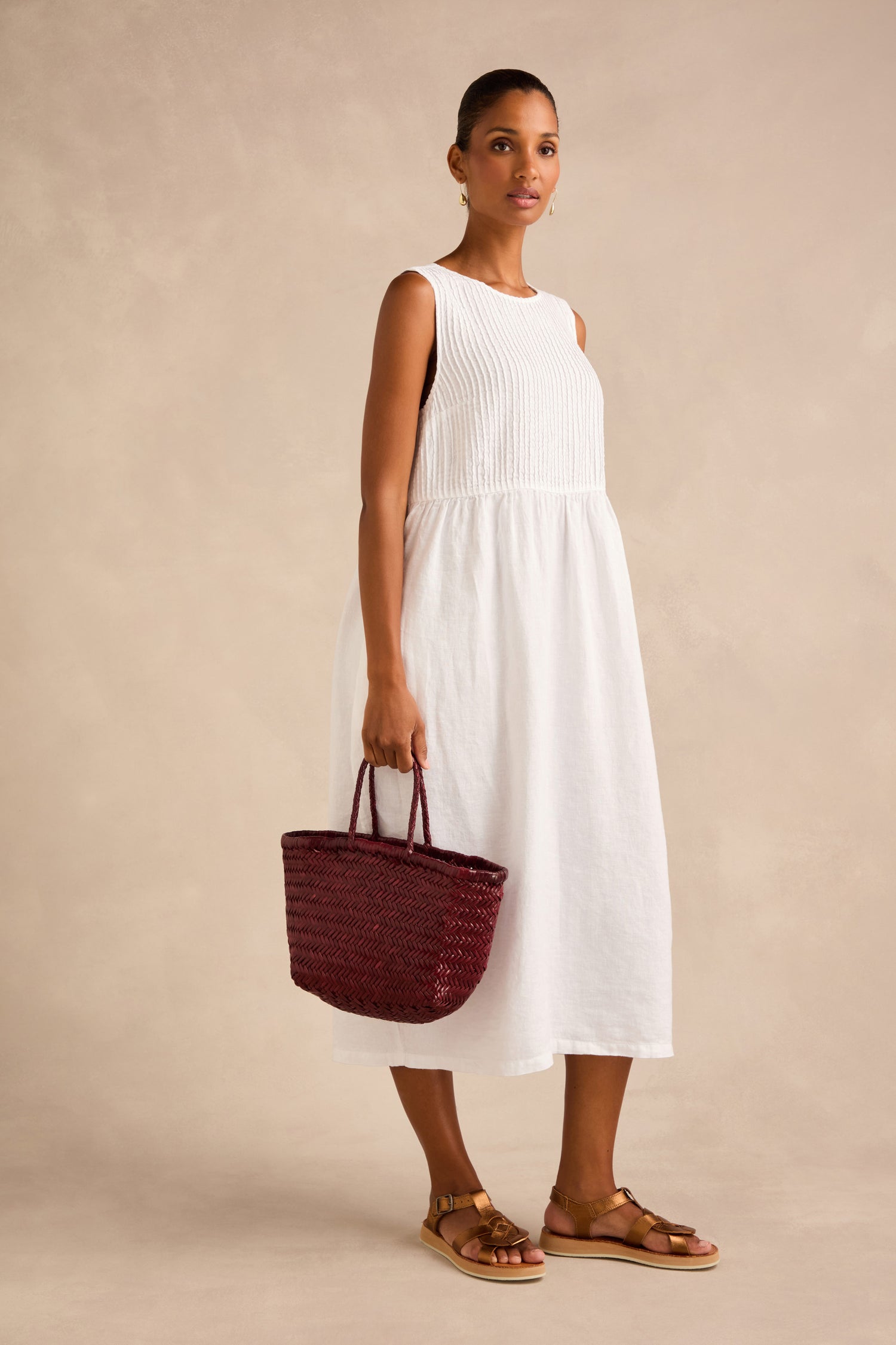 Woman in a sleeveless white midi dress holds a Small Triple Jump Woven Leather Bag and wears brown sandals, standing against a beige background.