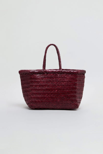 A dark red Small Triple Jump Woven Leather Bag with two handles sits against a plain light background. This beautiful piece from Dragon Diffusion highlights exquisite craftsmanship in every handwoven detail.