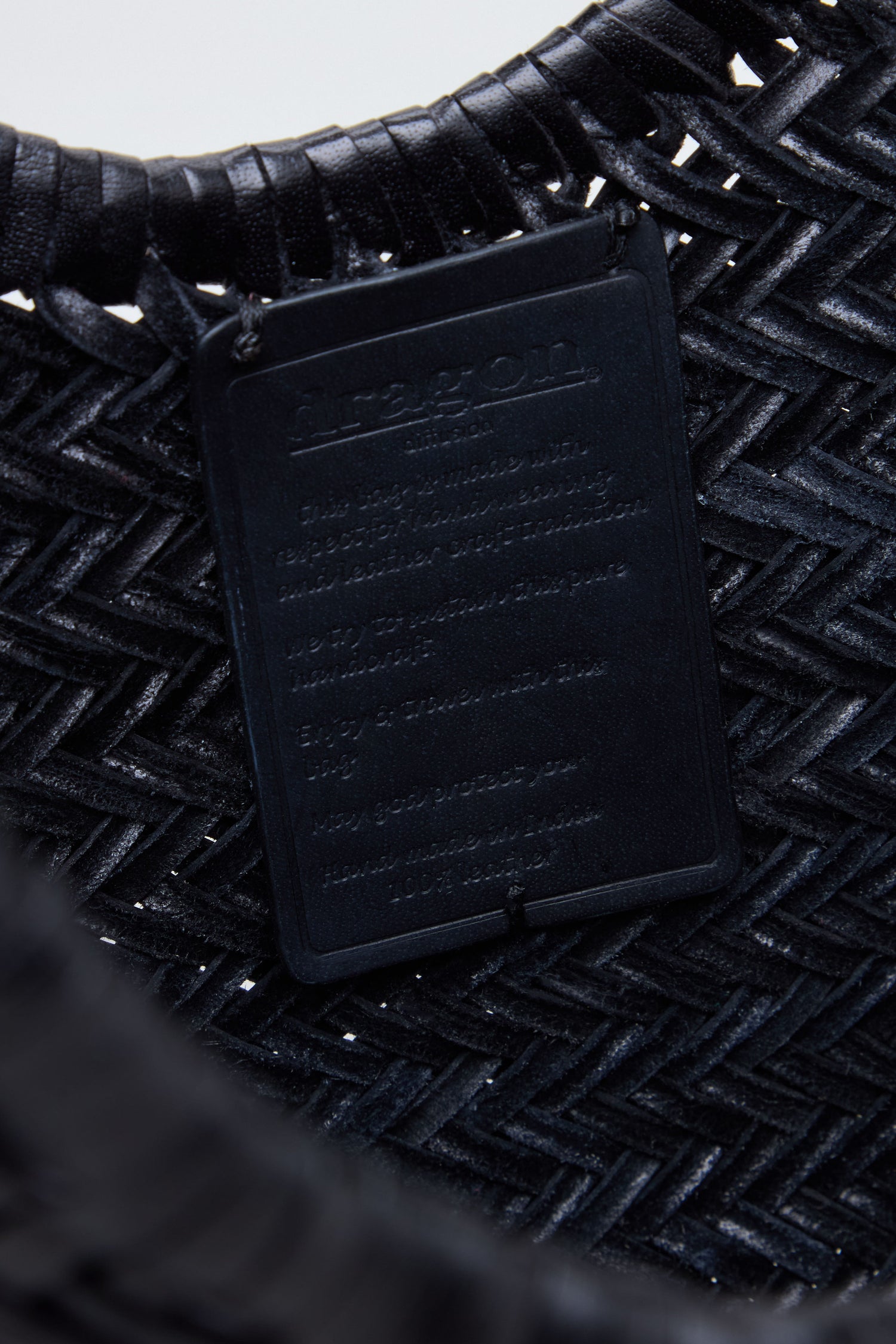Close-up of the Nantucket Woven Black Leather Bag, expertly handwoven from buffalo calf leather, featuring a rectangular black label with embossed text that is difficult to discern due to the lighting and angle.