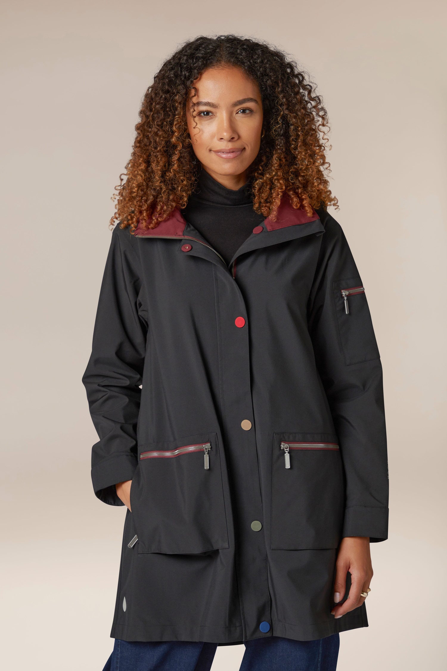 A woman wearing a storm-proof raincoat, specifically the 5 Pocket Hooded Rain Jacket, in black with red lining.