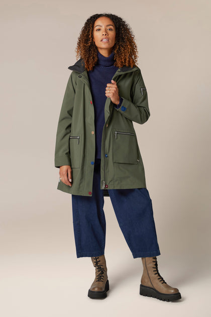 A woman wearing a 5 Pocket Hooded Rain Jacket in green with adjustable wrists, paired with jeans.