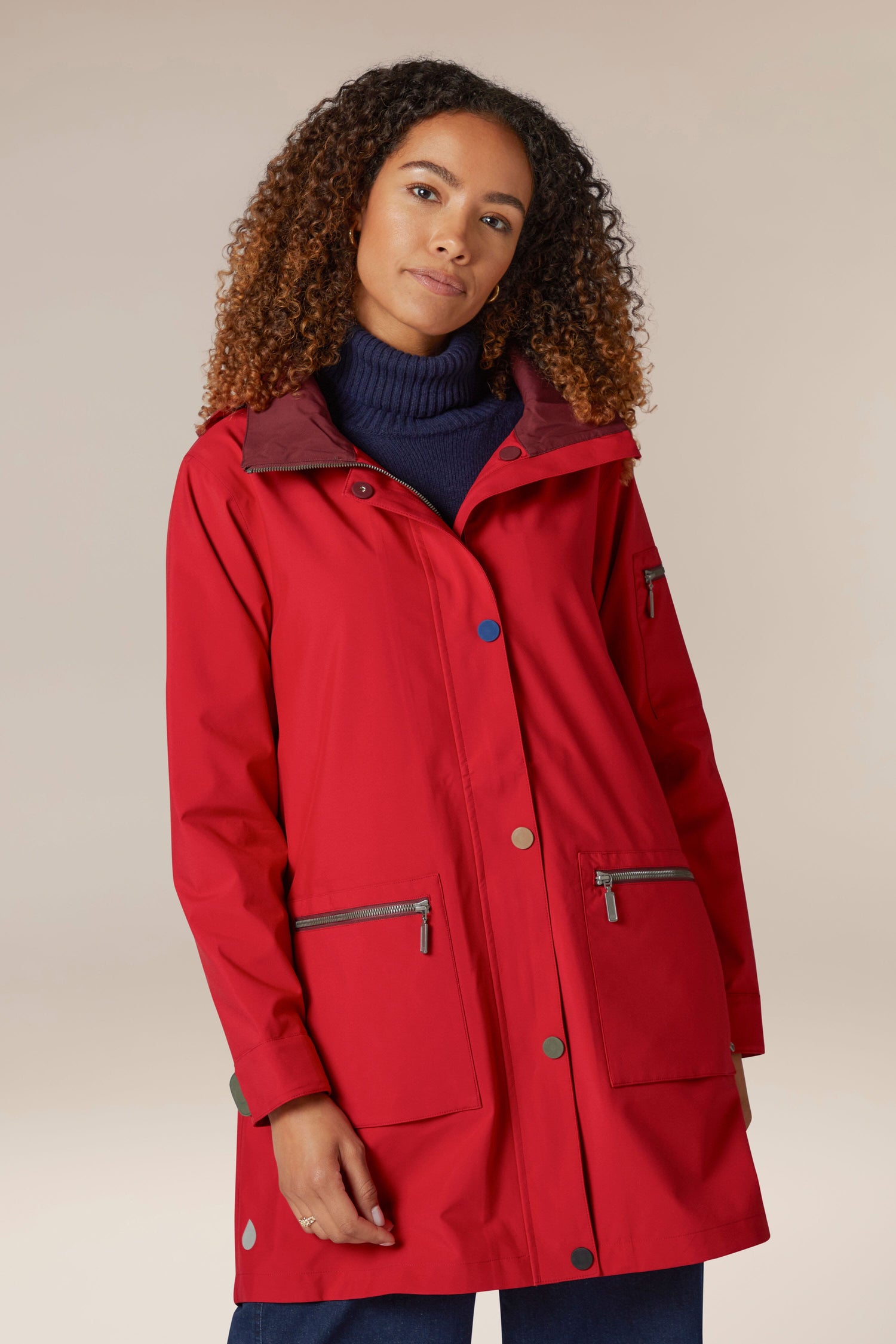 A woman wearing a 5 Pocket Hooded Rain Jacket with adjustable wrists in the color red.