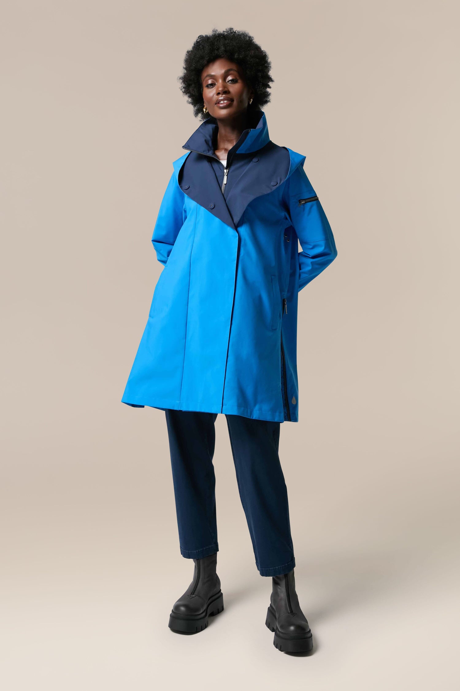 A woman wearing the Denise Wide Collar Rain Jacket from Scandi brand Regn, featuring black pants made from sustainability-accredited technical fabrics.