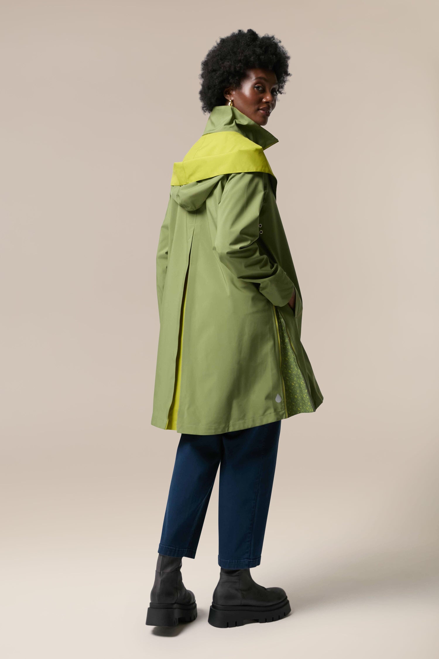 The back view of a woman wearing a storm-proof green raincoat, the Denise Wide Collar Rain Jacket by Scandi brand Regn.