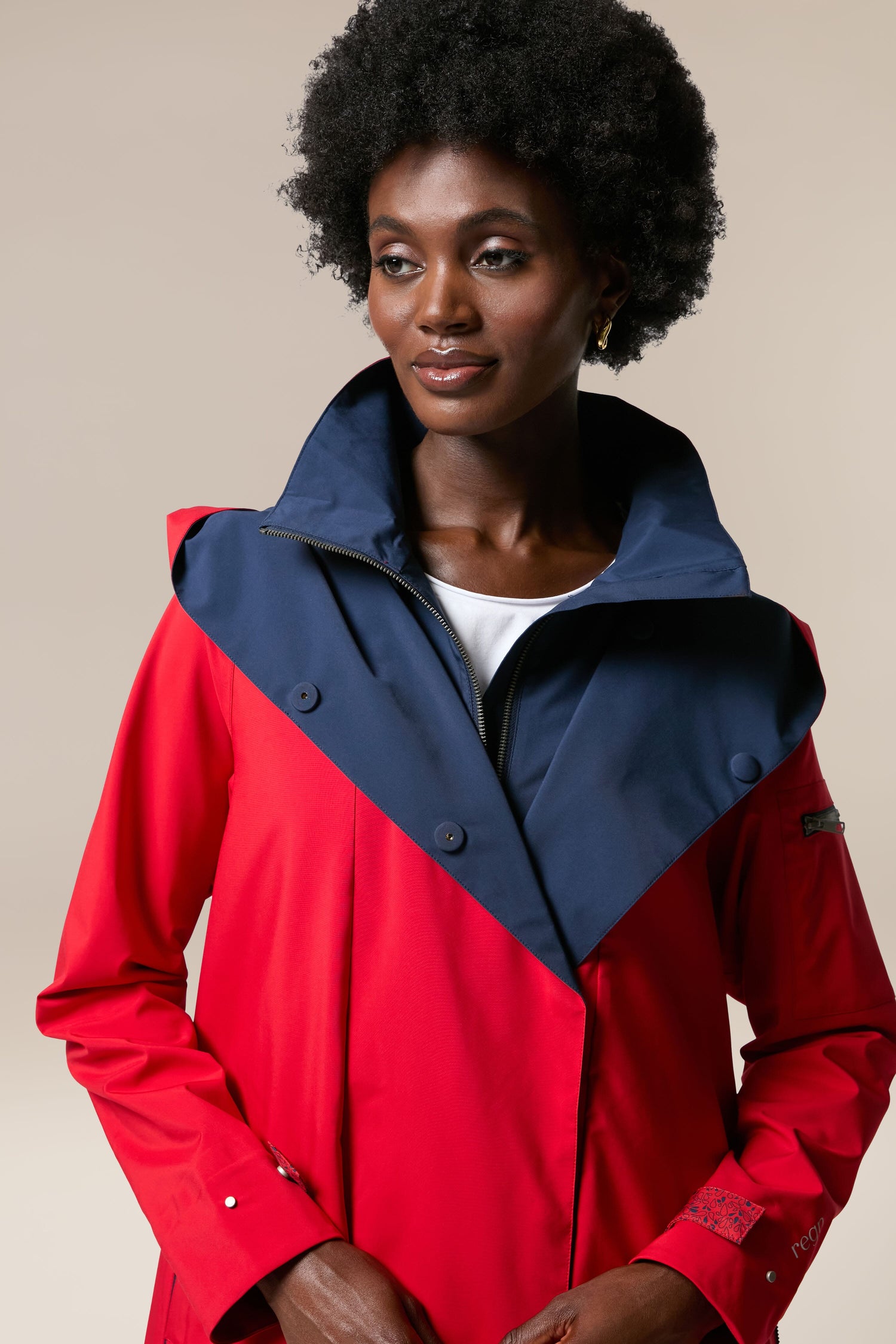 A woman donning a Denise Wide Collar Rain Jacket in storm-proof rainwear and sustainability-accredited technical fabrics in a red and navy coat.