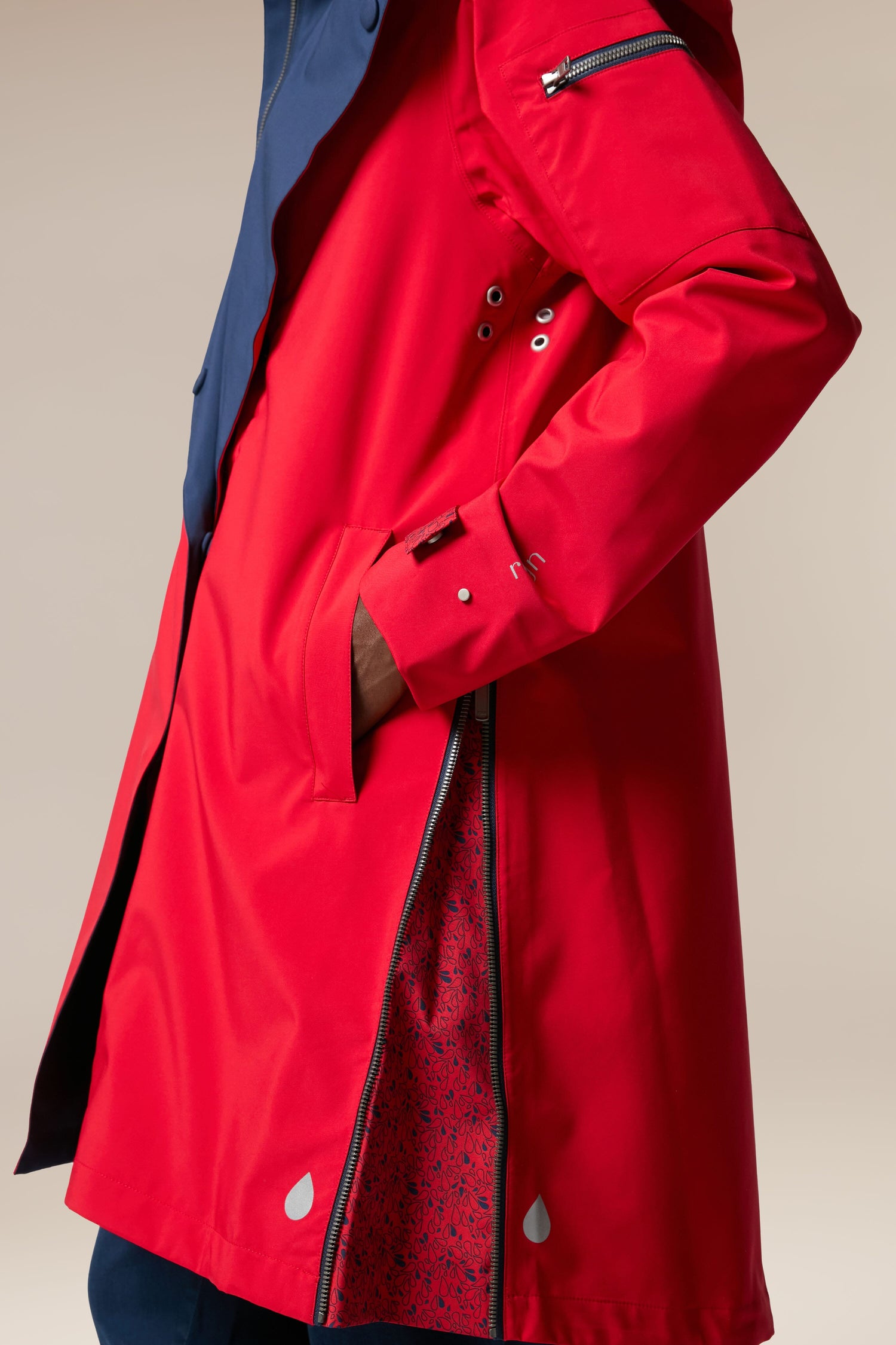 A woman is wearing storm-proof rainwear in a red raincoat with a blue hood, made with sustainability-accredited technical fabrics from the Scandi brand Denise Wide Collar Rain Jacket.