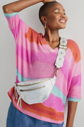 Person wearing a colorful striped sweater and blue pants poses with a Metallic Leather Crossbody Bag from Doris Maroquinerie.