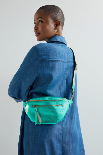A person in a blue coat and with a shaved head looks back, showing off an eye-catching Metallic Leather Crossbody Bag by Doris Maroquinerie.