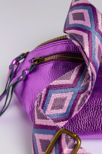 The Metallic Leather Crossbody Bag by Doris Maroquinerie is a close-up of an iridescent purple bag with a textured surface, featuring a zippered closure and a vibrant pink, purple, and blue strap with diamond shapes.