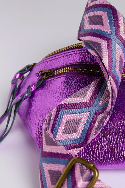 The Metallic Leather Crossbody Bag by Doris Maroquinerie is a close-up of an iridescent purple bag with a textured surface, featuring a zippered closure and a vibrant pink, purple, and blue strap with diamond shapes.