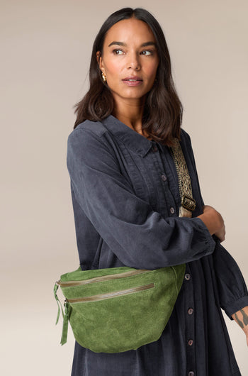 The Large Suede Crossbody Bag, made of metallic leather, is worn by a woman in a blue dress.
