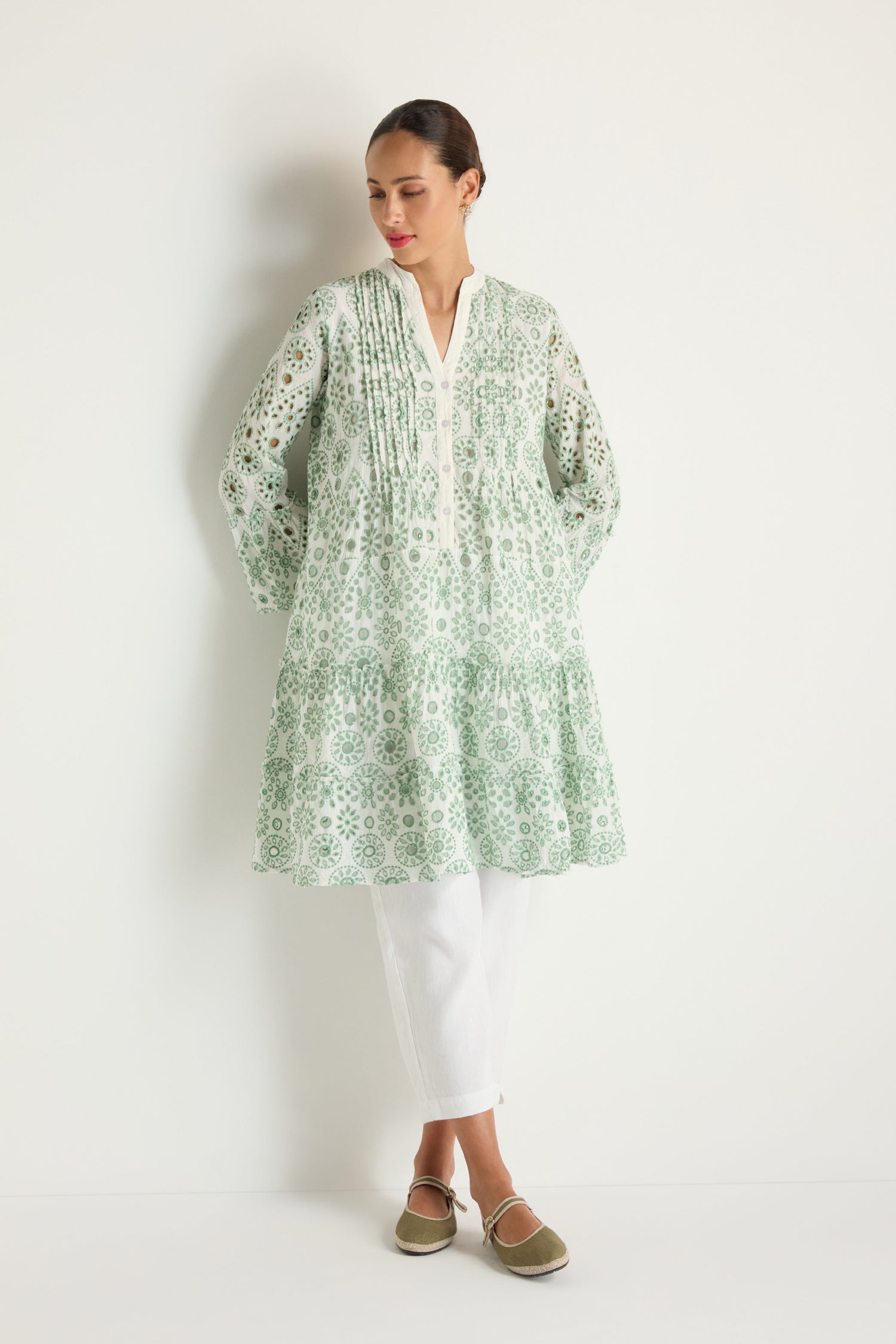 A woman wears the Embroidered Circle Flared Sleeve Tunic in light green and white, paired with white pants and green shoes, standing against a plain white background.
