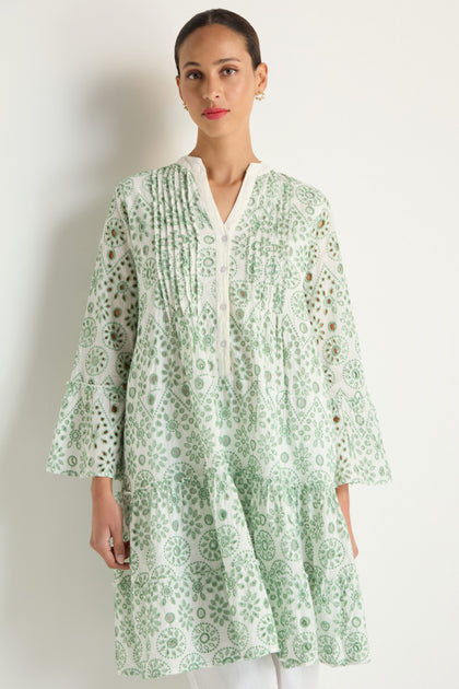 A woman models the Embroidered Circle Flared Sleeve Tunic in light green and white, featuring pleated details, white buttons, and Broderie anglaise embroidery, standing against a plain background.