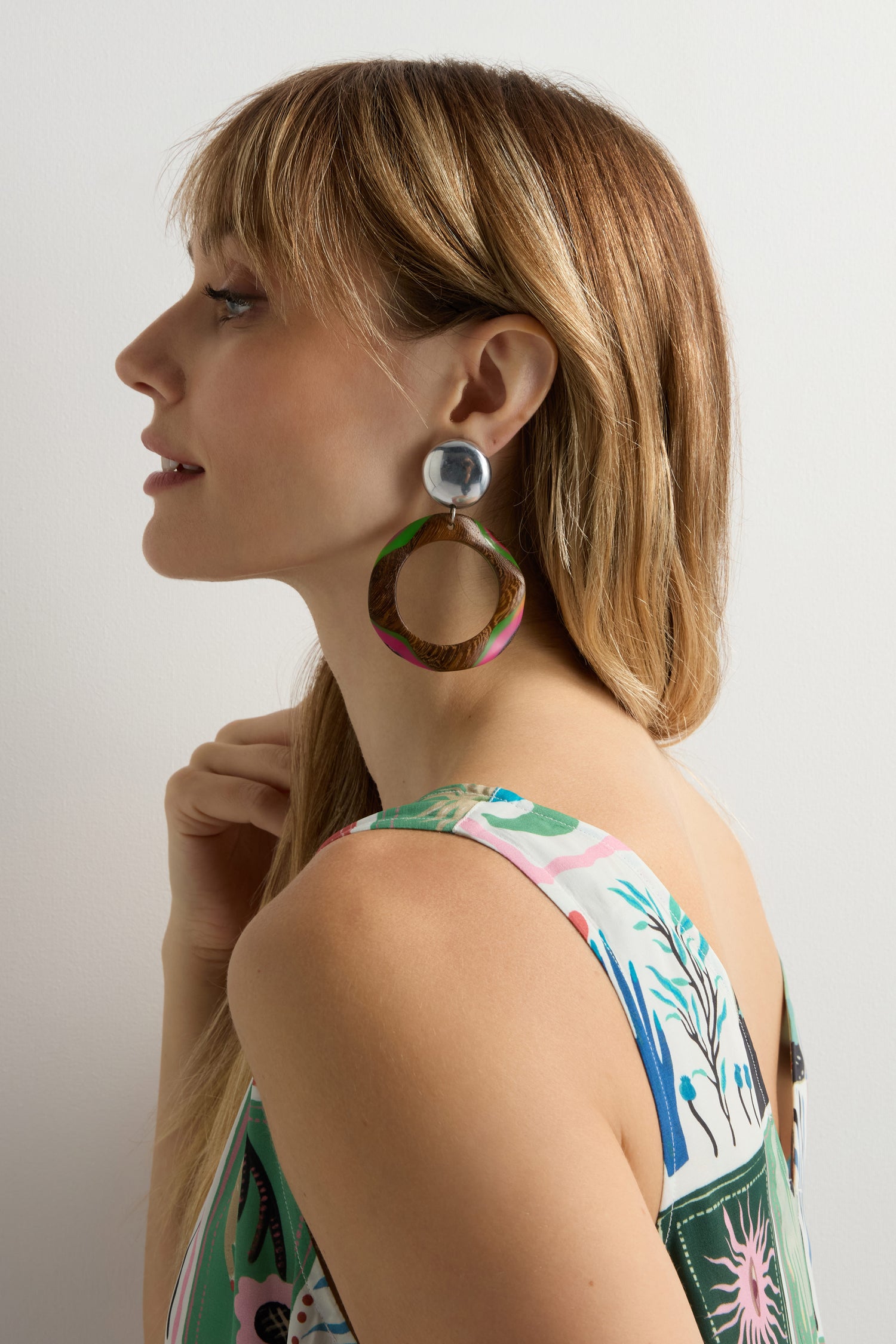 Woman with straight blonde hair wears Rainbow Spheres Clip-On Earrings and a colorful sleeveless top, looking left against a plain background.