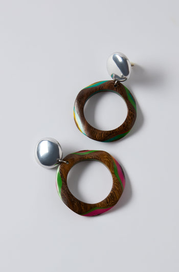 The Rainbow Spheres Clip-On Earrings feature round silver studs attached to oversized wooden hoops with irregular circular shapes and green and pink accents, shown on a plain white background.