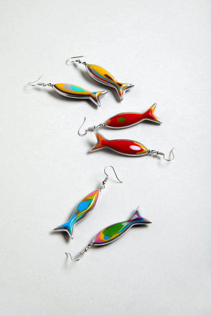 Six vibrant Poisson Earrings, crafted from multicolour resin in playful fish shapes with metal hooks, are displayed on a light grey surface.