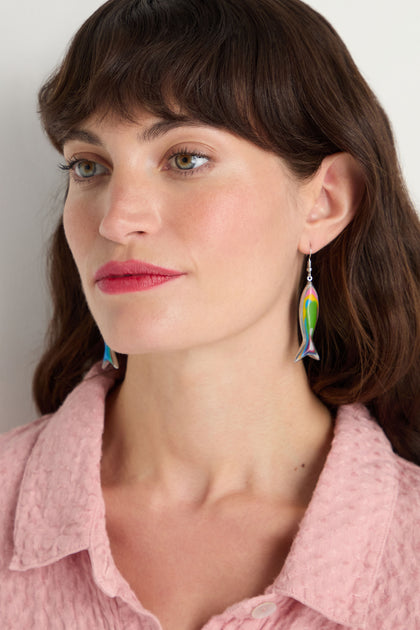 Fair-skinned woman with brown hair wears a pink textured top and vibrant Poisson Earrings—multicolour resin fish shapes—while looking slightly to the side.