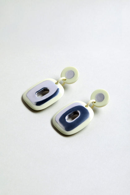 The Deco Earrings are geometric statement earrings with round studs and rectangular silver and cream accents, crafted from recycled aluminium and shown on a plain light background.