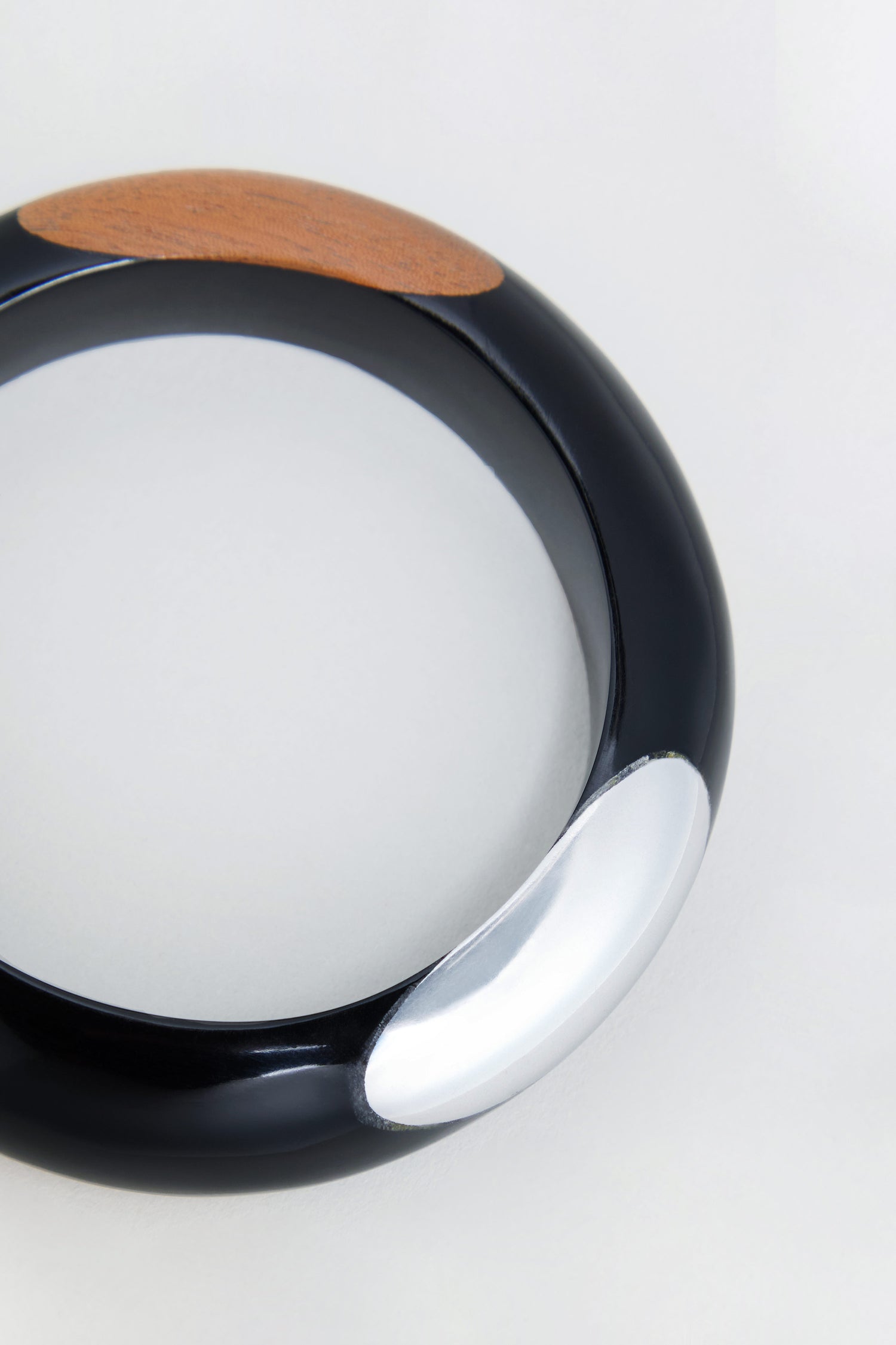 Introducing the Dotty Bangle: a round black wooden bangle featuring a distinctive wood accent and a bold silver aluminium detail, beautifully showcased against a light background.