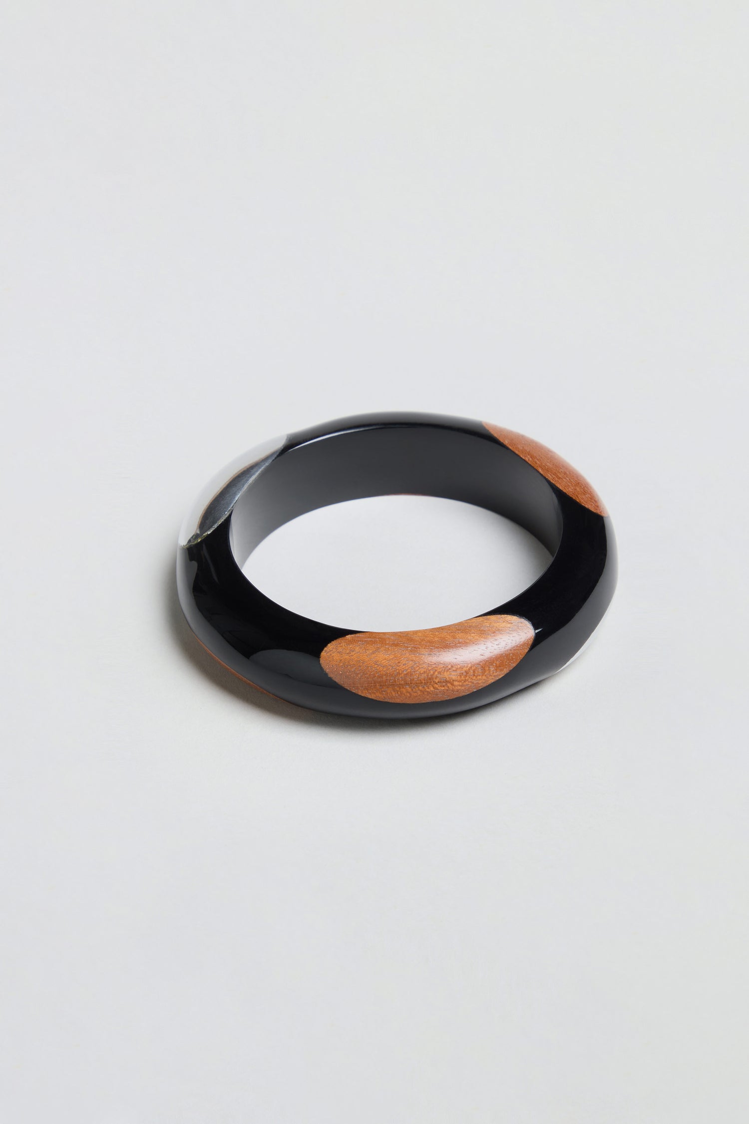 Dotty Bangle, a round statement accessory featuring alternating sections of black resin and light brown wood with a sleek aluminium accent, displayed on a plain light background.